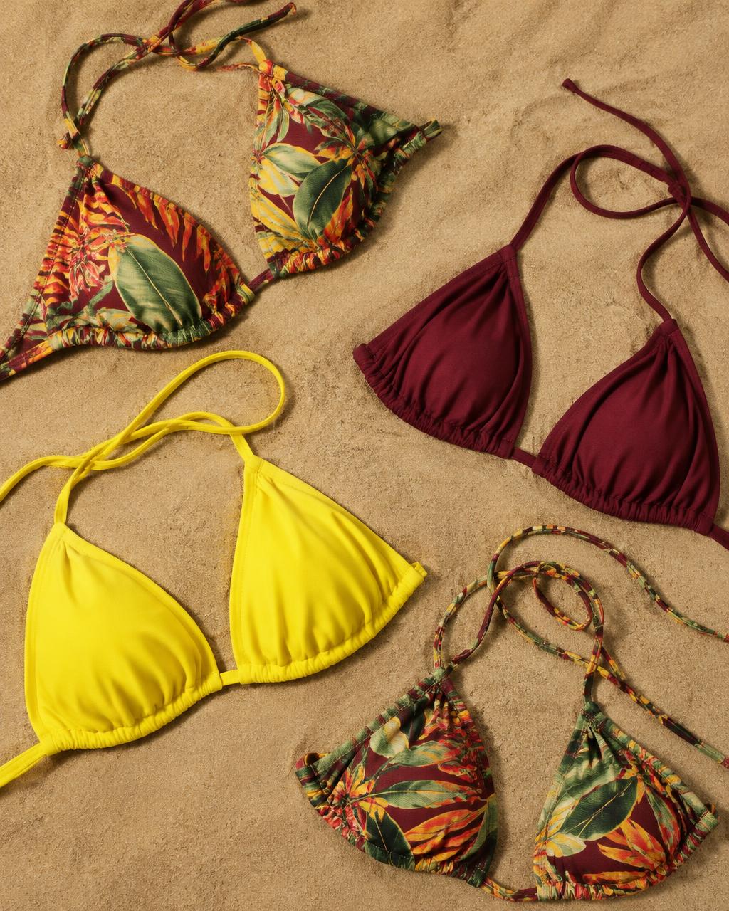 Tropical print and solid burgundy and yellow bikini tops on sand